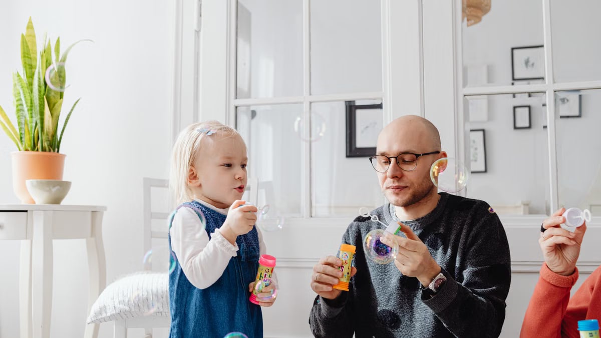 A joyful moment between a father and daughter blowing bubbles indoors, highlighting family fun.